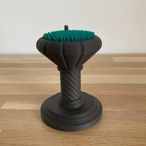 May include: A black, decorative pedestal with a green, textured top. The pedestal has a twisted column and a round base.