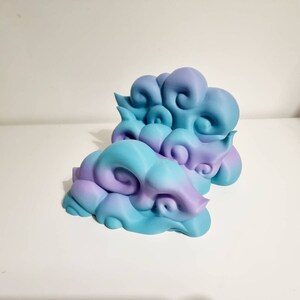 May include: Two decorative cloud sculptures in shades of blue and purple. The clouds have a swirling, textured design and are placed on a white surface. The sculptures are a unique home decor item.