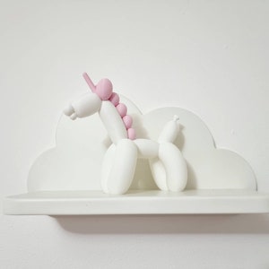 May include: White ceramic unicorn figurine with a pink mane and horn, sitting on a white cloud-shaped shelf.
