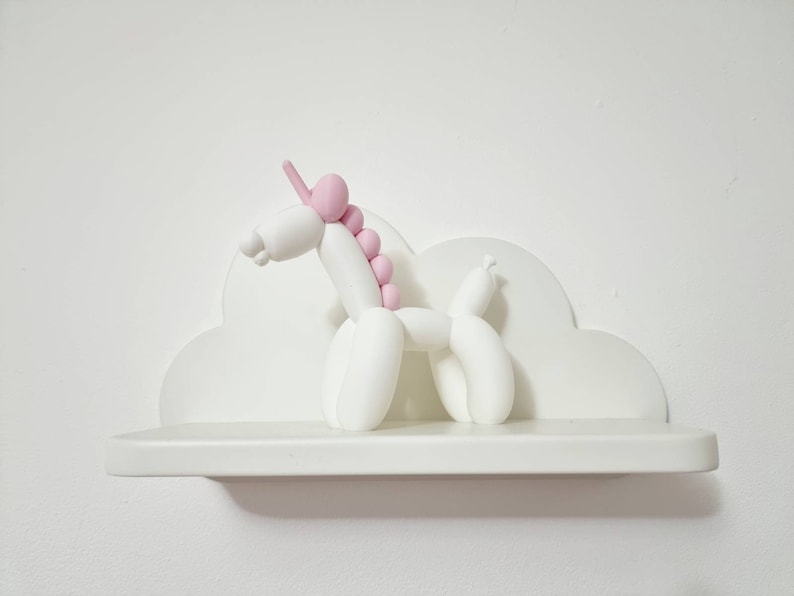 May include: White ceramic unicorn figurine with a pink mane and horn, sitting on a white cloud-shaped shelf.
