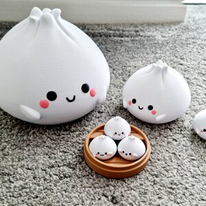 May include: A set of four white, cartoon-style steamed buns with happy faces. The buns are arranged in a bamboo steamer, with three smaller buns and one larger bun.