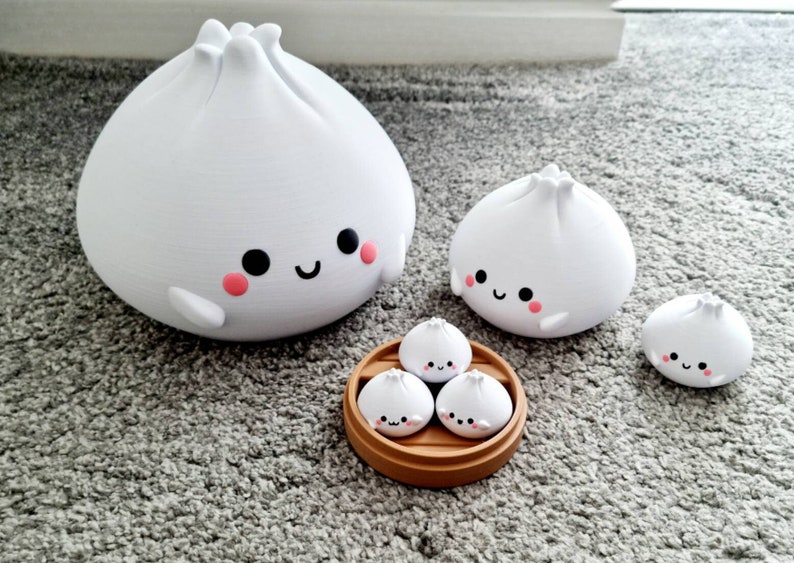 May include: A set of four white, cartoon-style steamed buns with happy faces. The buns are arranged in a bamboo steamer, with three smaller buns and one larger bun.