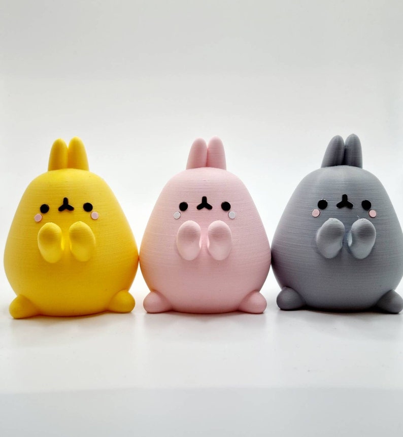 K&ouml;nnte beinhalten: Drei kleine Pl&uuml;schtiere in Form von Hasen mit unterschiedlichem Fell. Der Hase links ist gelb, der mittlere Hase ist rosa und der Hase rechts ist grau. Jeder Hase hat eine kleine, schwarze Nase und Augen sowie einen kleinen, schwarzen Mund.