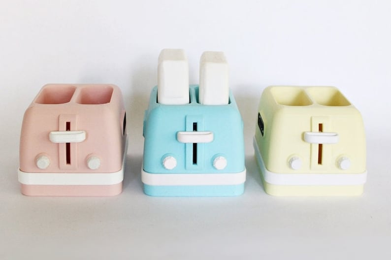 K&ouml;nnte beinhalten: Drei Miniatur-Toaster in Rosa, Blau und Gelb. Jeder Toaster hat zwei Schlitze und einen wei&szlig;en Hebel.