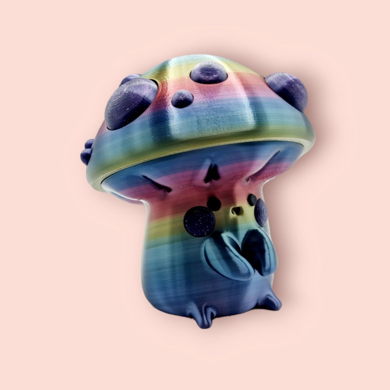 May include: A rainbow-colored mushroom figurine with a whimsical design. The mushroom has a wide, flat cap with a textured surface and a small, round stem. The cap is decorated with purple dots and the stem has a blue and purple swirl pattern.
