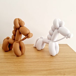 May include: Two balloon animal sculptures, one brown and one white, shaped like horses with reins. The sculptures are on a wooden surface.