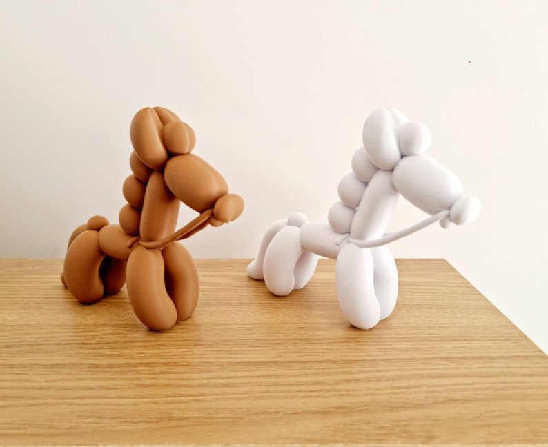 May include: Two balloon animal sculptures, one brown and one white, shaped like horses with reins. The sculptures are on a wooden surface.