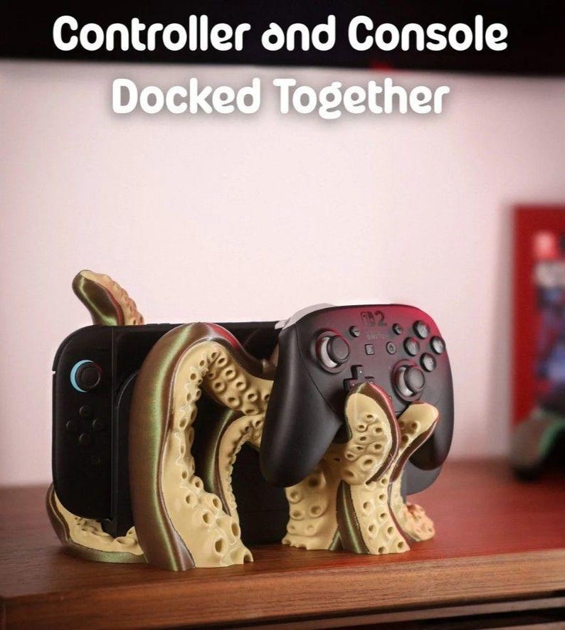 May include: A black game console and controller are docked together in a unique stand. The stand is designed with an octopus-like tentacle motif in tan and brown colors. The text "Controller and Console Docked Together" is displayed at the top.