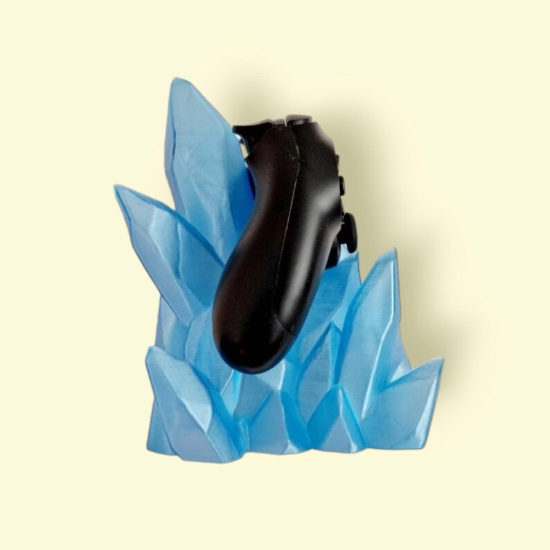 May include: A black video game controller is held in a blue crystal-shaped stand. The stand is made to look like ice.