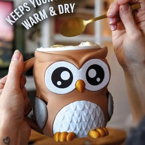 May include: A brown owl-shaped mug with large black and white eyes, an orange beak, and white chest feathers. The mug has a handle and is being filled with a spoon. Text on the image reads "KEEPS YOUR HANDS WARM & DRY."