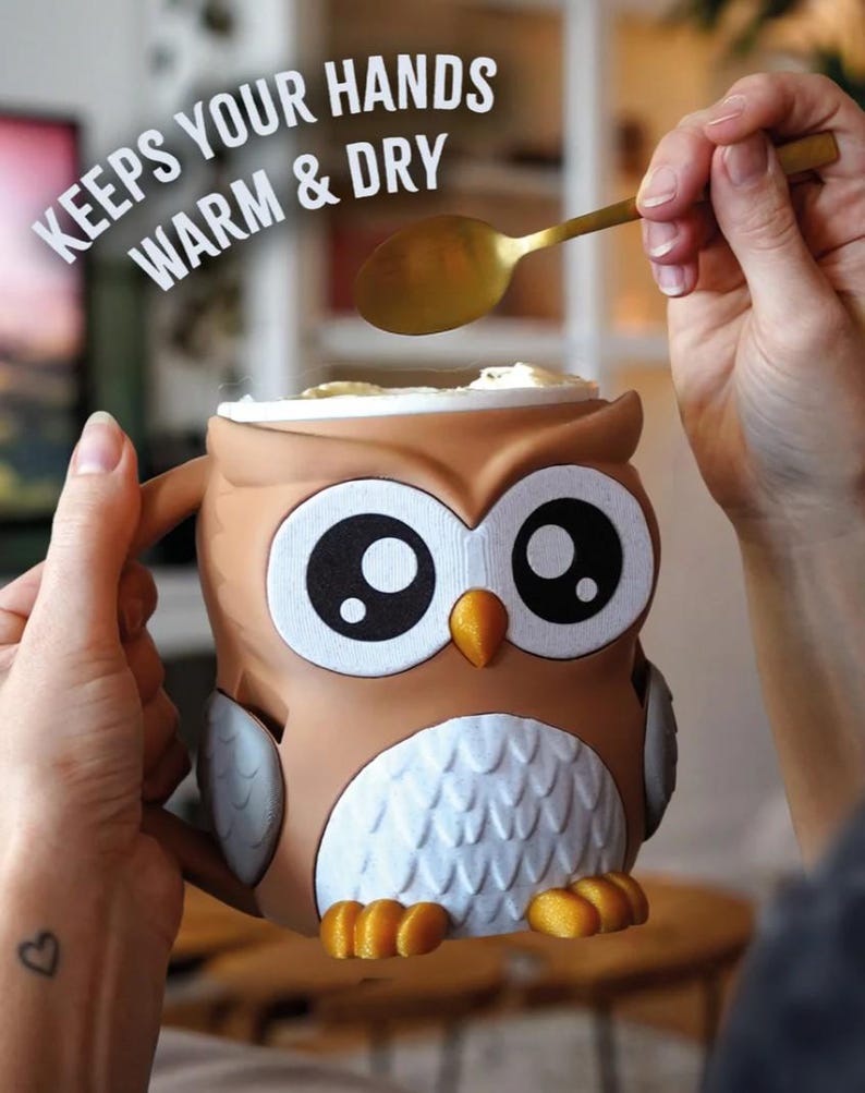 May include: A brown owl-shaped mug with large black and white eyes, an orange beak, and white chest feathers. The mug has a handle and is being filled with a spoon. Text on the image reads "KEEPS YOUR HANDS WARM & DRY."