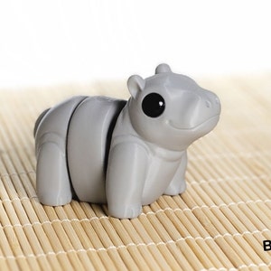May include: A gray, segmented, 3D printed toy hippopotamus with large black eyes. The toy is sitting on a bamboo mat.