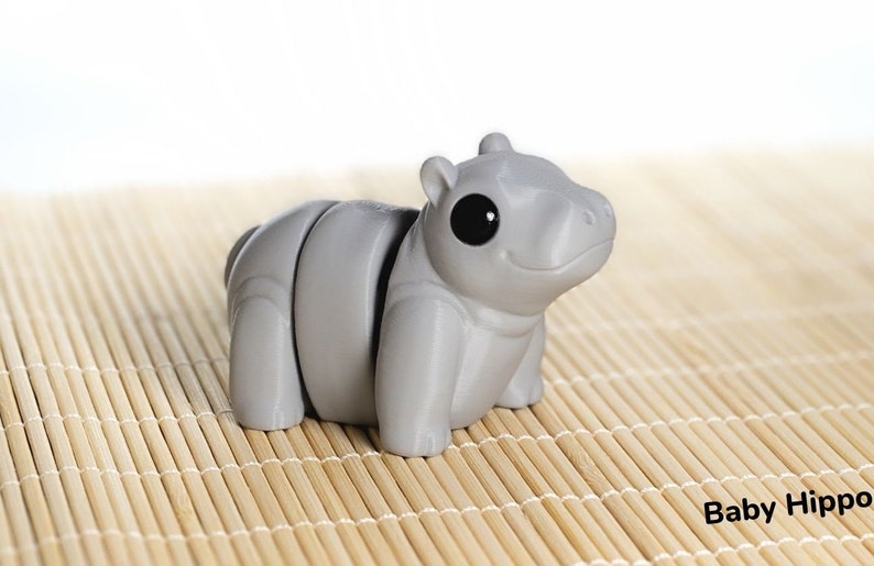 May include: A gray, segmented, 3D printed toy hippopotamus with large black eyes. The toy is sitting on a bamboo mat.