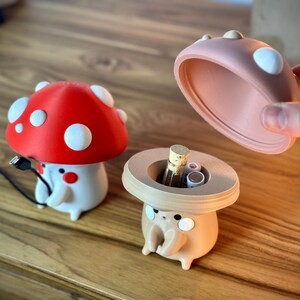 May include: Two mushroom-shaped containers, one red with white dots and one brown with a beige lid. The brown mushroom container is open and has batteries inside.