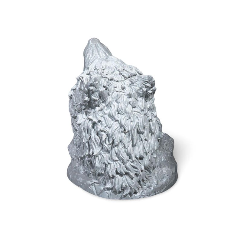 May include: A silver-colored sculpture of a bear's head, angled upwards. The bear's fur is detailed with textured lines, and the sculpture is set against a white background. The bear's head is the primary focus.