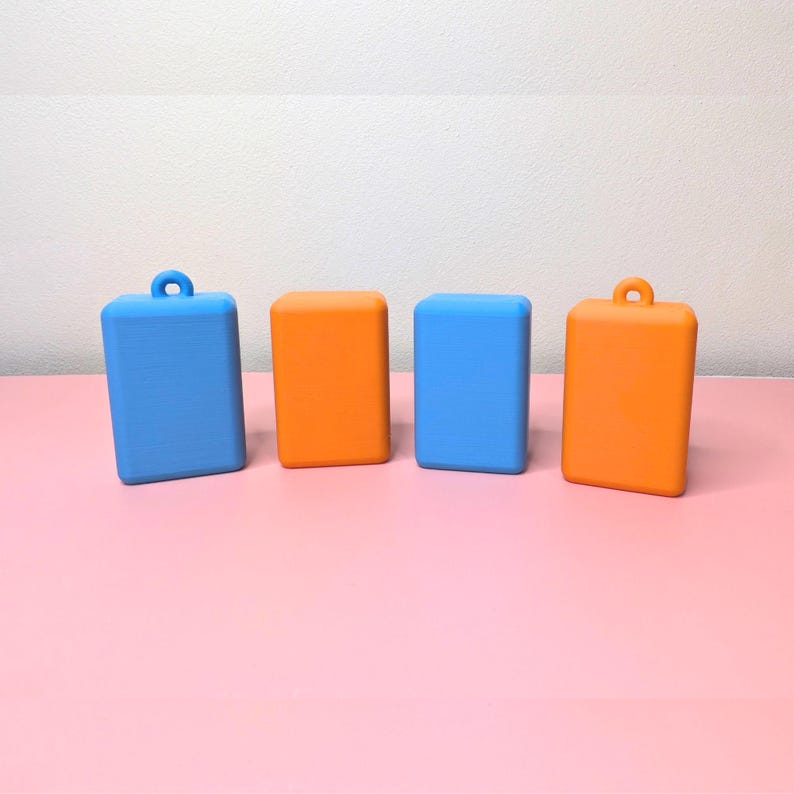 May include: Four rectangular, solid-colored objects. Two are blue, and two are orange. Each has a rounded top and bottom. Two have a small loop at the top. The objects are arranged on a pink surface.