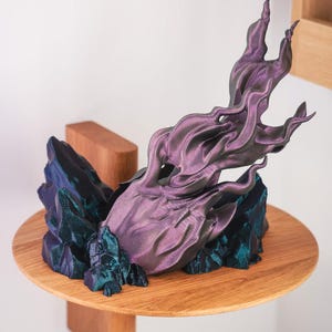 May include: A 3D printed sculpture of a purple and teal flame rising from a base of teal crystals. The sculpture is on a wooden shelf.