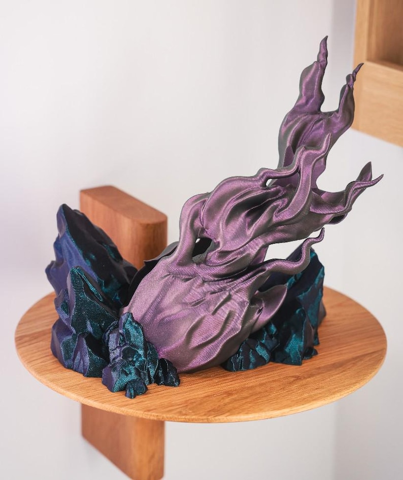 May include: A 3D printed sculpture of a purple and teal flame rising from a base of teal crystals. The sculpture is on a wooden shelf.