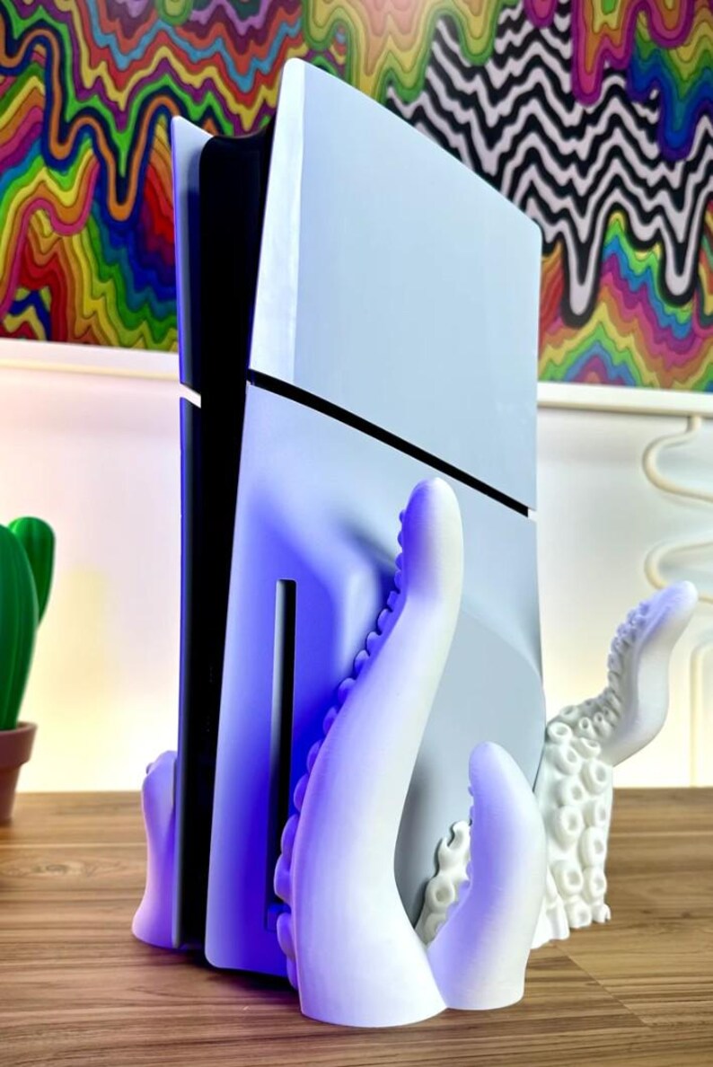 May include: A white 3D printed octopus stand for a video game console. The stand has two tentacles on the left and one on the right. The console is white and black and is held in place by the tentacles.