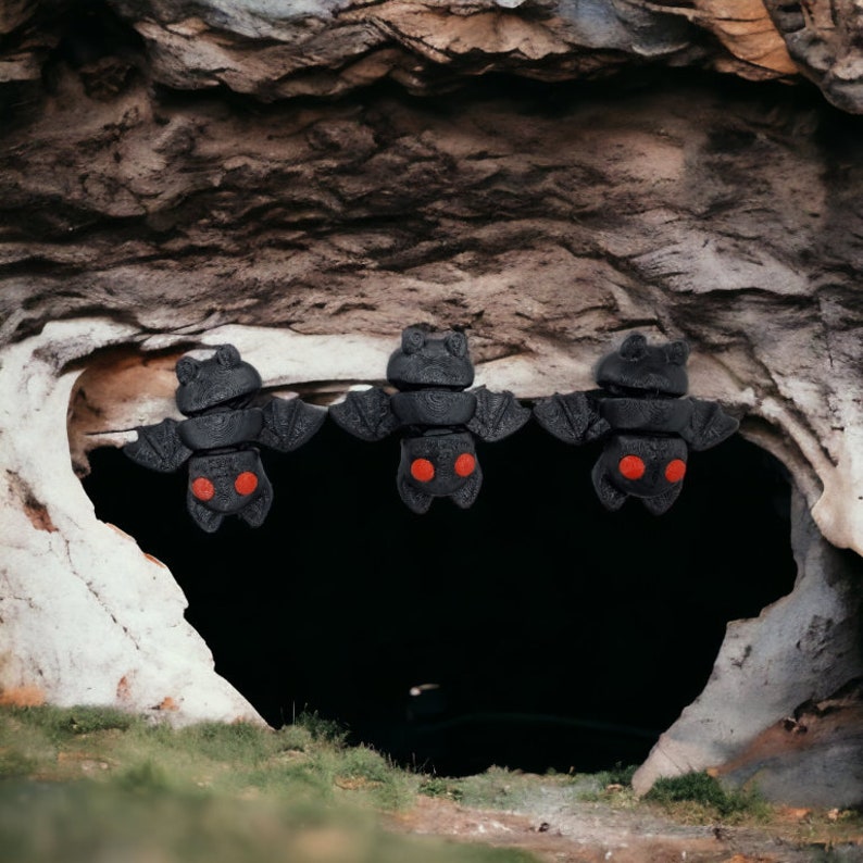 May include: Three black bats with red eyes hanging upside down from a cave opening. The bats are made of a soft, pliable material.