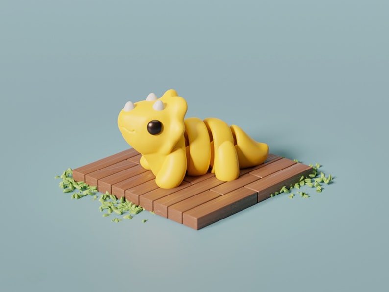 May include: A yellow, cartoon-style triceratops dinosaur figurine sits on a wooden platform with green grass scattered around it.