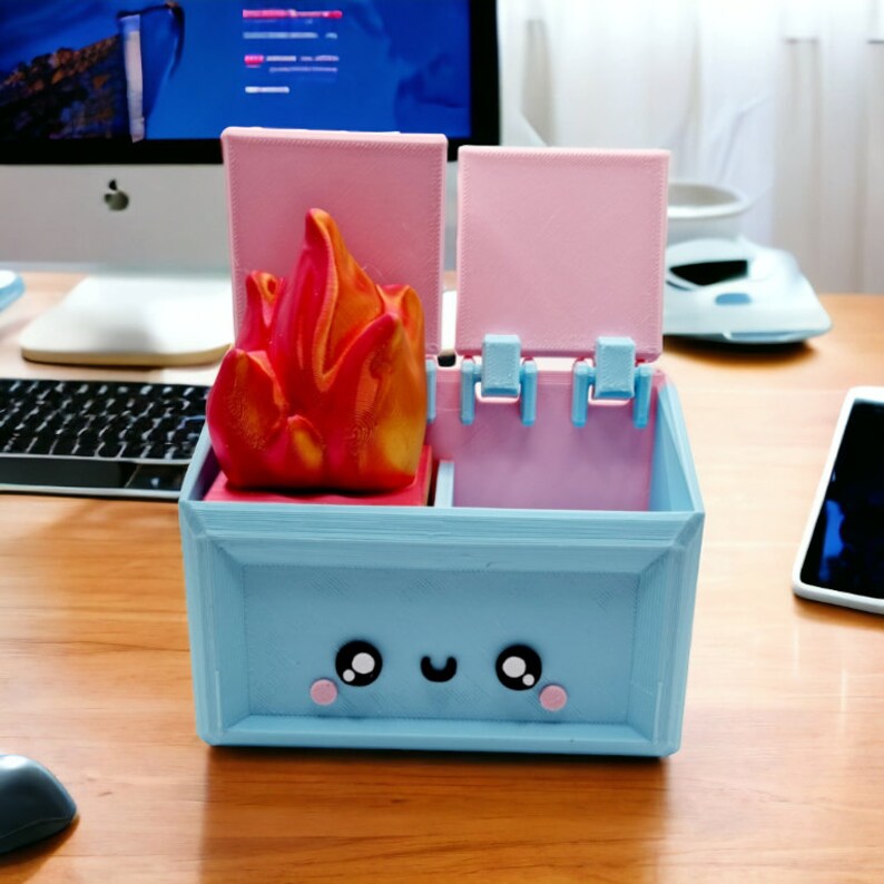 May include: A blue and pink 3D printed box with a smiling face. The box has two compartments with lids that open. The top compartment has a red and orange 3D printed flame inside.
