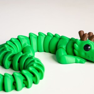 May include: A green segmented dragon figurine with brown antlers and large black eyes. The dragon is curled up in a sleeping position.