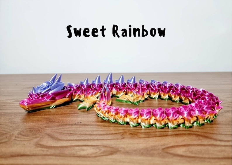Peut inclure: Un dragon color&eacute;, aux couleurs de l'arc-en-ciel, fait de papier origami. Le dragon est enroul&eacute; sur une surface en bois. Le texte "Sweet Rainbow" est &eacute;crit au-dessus du dragon.