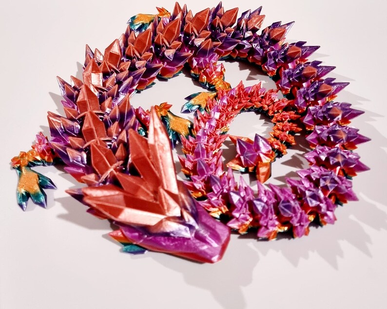 May include: A colorful, iridescent dragon sculpture made of faceted crystals. The dragon is curled up in a circle, with its head resting on its tail. The sculpture is made of a variety of colors, including red, orange, yellow, green, blue, and purple.