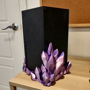 Puede incluir: Una consola de juegos negra con una base de cristal morado. La consola est&aacute; sentada sobre una superficie de madera.