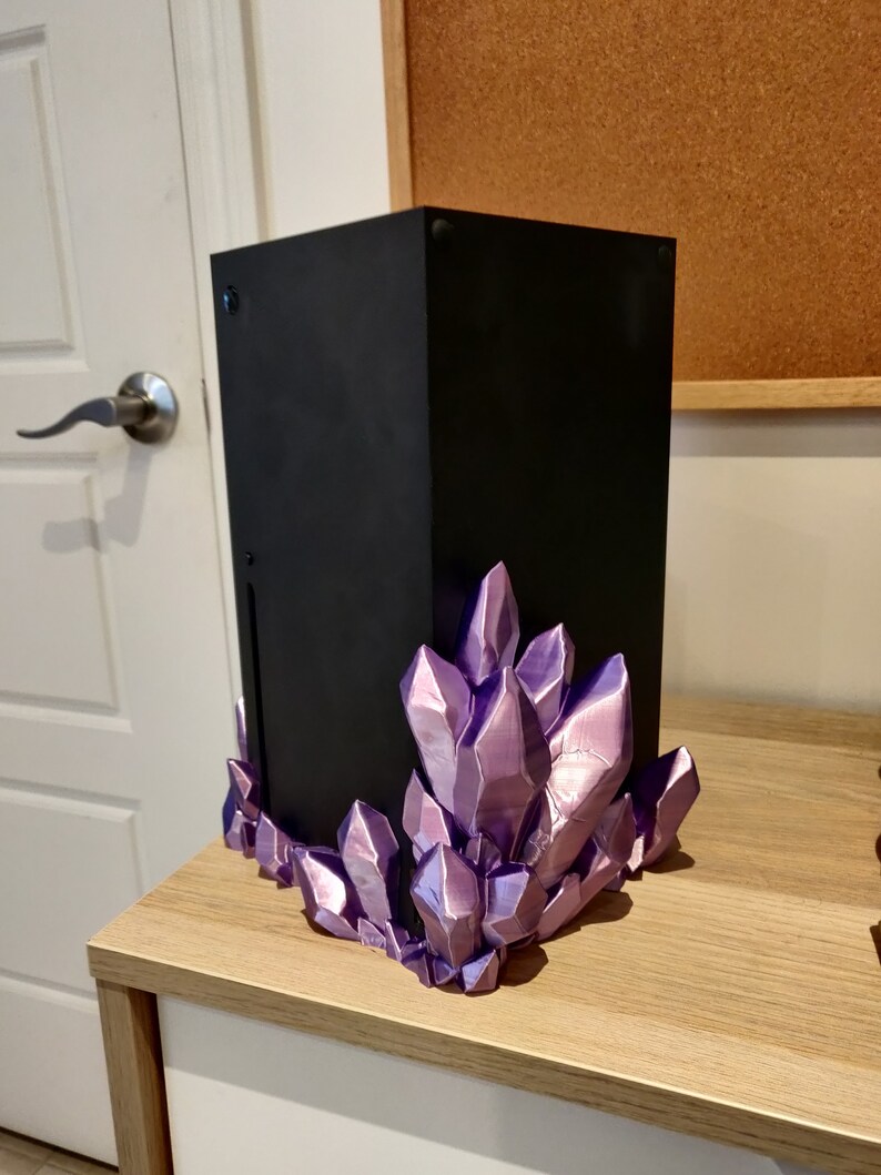 Puede incluir: Una consola de juegos negra con una base de cristal morado. La consola est&aacute; sentada sobre una superficie de madera.