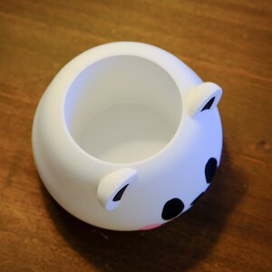 May include: White ceramic planter shaped like a bear's face with black eyes and a pink nose.