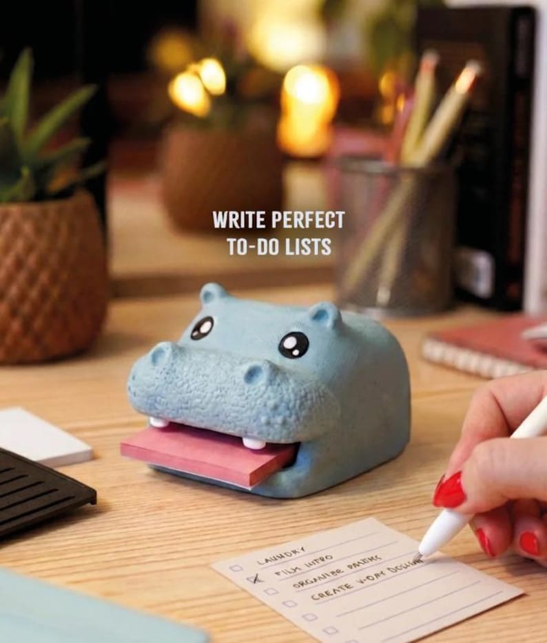 May include: A light blue hippo-shaped sticky note holder with a pink pad of sticky notes. The text "WRITE PERFECT TO-DO LISTS" is visible. A person is writing on a to-do list.