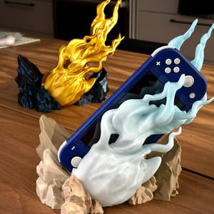 May include: A blue Nintendo Switch console is held in a 3D printed stand shaped like a blue flame. The stand is on a wooden surface.