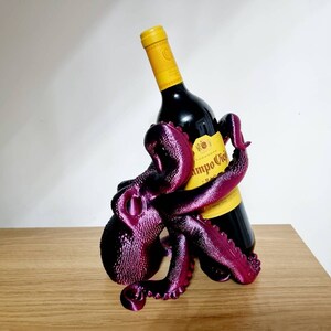 May include: A purple octopus-shaped wine bottle holder with a bottle of red wine inside. The bottle label reads "Campo Viejo Rioja".
