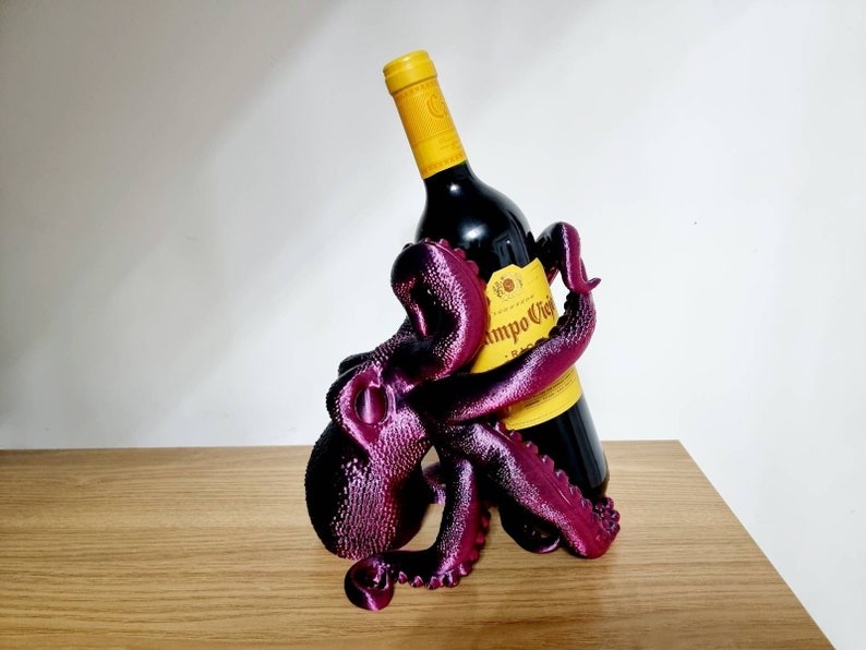 May include: A purple octopus-shaped wine bottle holder with a bottle of red wine inside. The bottle label reads "Campo Viejo Rioja".