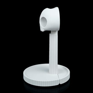 May include: A white, modern-style paper towel holder. The holder features a circular base, a vertical support with a ridged texture, and a curved top section designed to hold the paper towels. The design is minimalist and sleek.