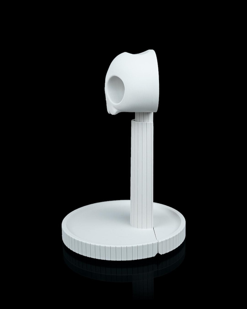 May include: A white, modern-style paper towel holder. The holder features a circular base, a vertical support with a ridged texture, and a curved top section designed to hold the paper towels. The design is minimalist and sleek.