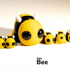 May include: A group of yellow and black bee figurines with large eyes. The largest bee is in the center and has white antennae. The text "Baby Bee" is written below the figurines.