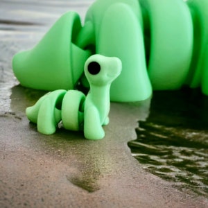 Pu&ograve; includere: Un bruco di giocattolo verde segmentato con un bruco di giocattolo verde pi&ugrave; piccolo con occhi neri attaccato alla sua schiena.