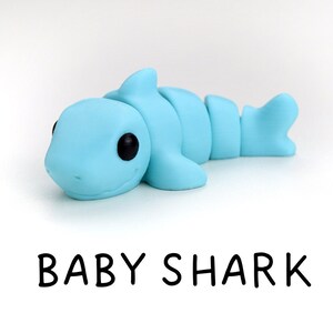 May include: A light blue baby shark figurine made of clay. The shark has black eyes and a small mouth.