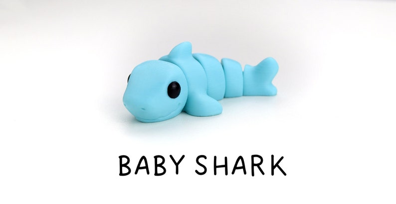 May include: A light blue baby shark figurine made of clay. The shark has black eyes and a small mouth.