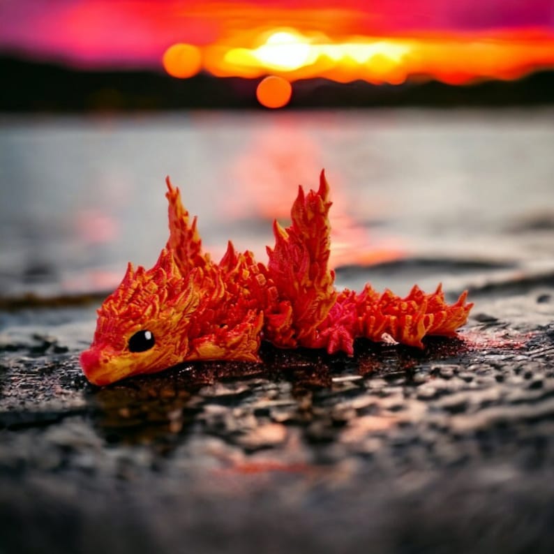 May include: A small, orange and red, fire-like creature with a spiky back and a cute face. The creature is lying on a dark, textured surface.