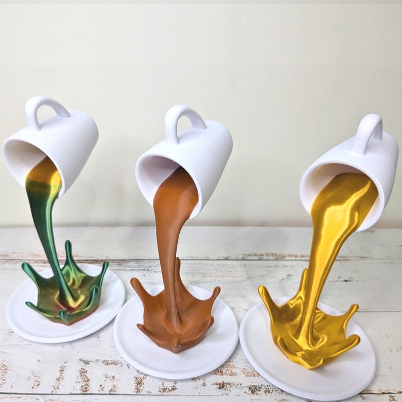 May include: Three white ceramic coffee cups with handles, each tilted to pour a liquid onto a white saucer. The liquids are green, brown, and gold, creating a splash effect. The cups are on a white wooden surface.