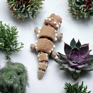 May include: A brown and white segmented toy lizard with a textured surface. The toy is posed on a white background with green plants.