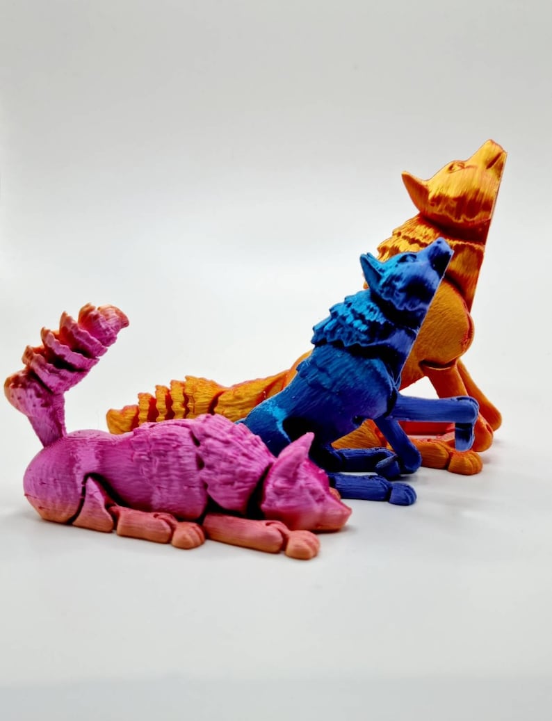 May include: Three 3D printed wolf figurines in different poses. The wolf on the left is pink, the middle wolf is blue, and the wolf on the right is orange.
