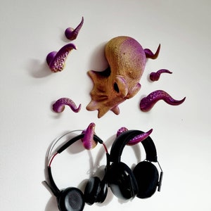 May include: Purple and gold octopus wall hooks with tentacles. Two black headphones are hanging on the hooks.