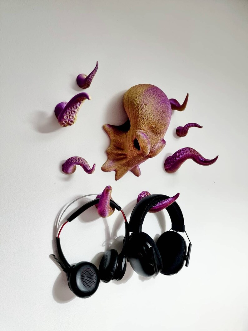 May include: Purple and gold octopus wall hooks with tentacles. Two black headphones are hanging on the hooks.