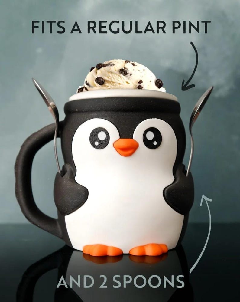 May include: A black, white, and orange penguin-shaped mug with two spoons. The mug is filled with ice cream. Text on the image reads "FITS A REGULAR PINT AND 2 SPOONS."