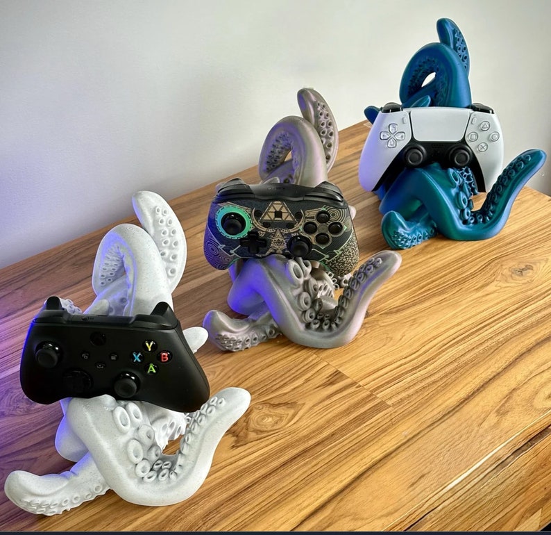 May include: Three 3D printed octopus-shaped stands, each holding a different video game controller. The stands are printed in white, teal, and gray. The controllers are black, white, and black and green.